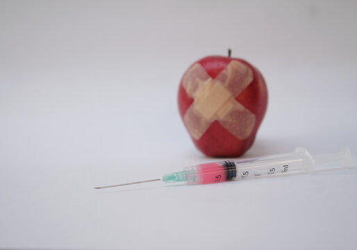 Jeringa con dosis unica para tratamiento m&eacute;dico, con un fondo blanco y una manzana en mal estado.