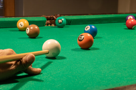 Jogador de sinuca mirando o taco para acertar a bola branca em dire&ccedil;&atilde;o &agrave; bola 13 verde na boca da ca&ccedil;apa