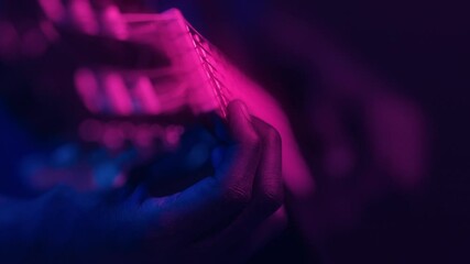 African American man plays an electric guitar, surrounded by vibrant neon hues. The atmosphere is that of a cool, modern space, emphasizing creativity and passion for music.