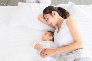 Asian young mother lullaby newborn baby on bed, tired single mom lying down next to adorable infant...