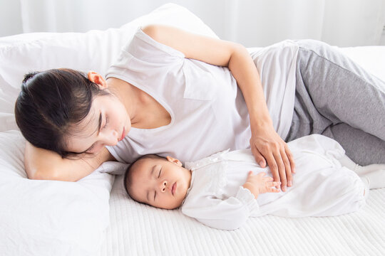 Asian young mother lullaby newborn baby on bed, tired single mom lying down next to adorable infant with tender. Women and toddlers 0-1 month sleeping, nurturing moment in soft natural lighting.