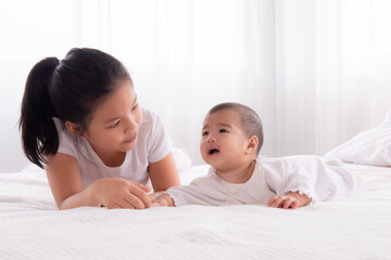 Asian siblings love bonding relationship, adorable younger sister playing with toddler baby on bed soft touching, happy kid nursing hugging embracing together, preschool girl spend the holiday at home