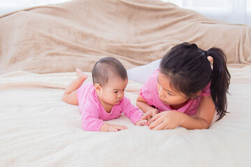 Asian siblings love bonding relationships, younger sister playing and teases toddler baby on bed...