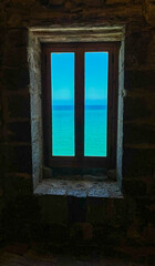 A stunning view of the turquoise sea through a rustic stone window, blending the old-world charm of the castle with the refreshing beauty of the ocean beyond.