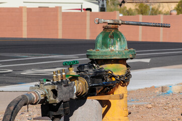 Close-up of a weathered green and yellow fire hydrant equipped with a secured hose and fittings,...