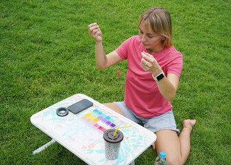 Young woman beading colorful bracelets outdoors in a park