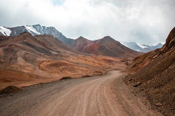 A dirt road winds through a desert with snow-capped mountains in the background