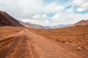 A dirt road in the desert with a cloudy sky in the background