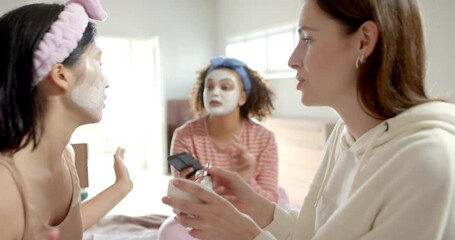 Applying face masks, three diverse women friends enjoying skincare routine together at home - Powered by Adobe