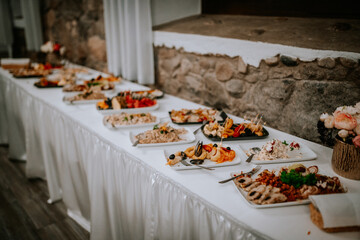 A long buffet table with assorted dishes, including seafood, salads, and appetizers, elegantly displayed on white tablecloths at an event.