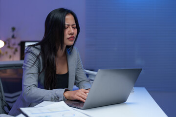 Young professional woman feeling tired and stressed while using laptop computer and working late night in office, experiencing burnout and frustration from overwork