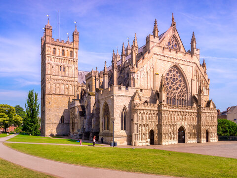  Exeter, Devon, UK - The Cathedral Church of St Peter, Exeter, Devon, the seat of the Bishop of Exeter, with people walking and relaxing around Cathedral Green on a summer afternoon. 