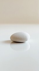A single smooth stone on a reflective surface, embodying simplicity and calmness in a minimalist setting.
