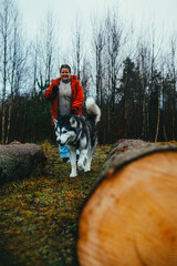 A woman in a red jacket walking with an Alaskan Malamute near fa
