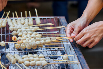 Cropped hand of people grilling skewers meatball on barbecue grill