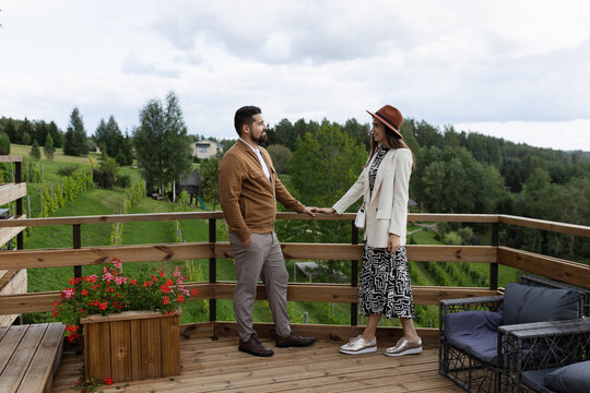 Stylish couple standing on terrace holding hands with vineyard behind