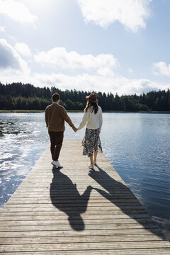 Young adult couple walking on pier by the lake and holding hands