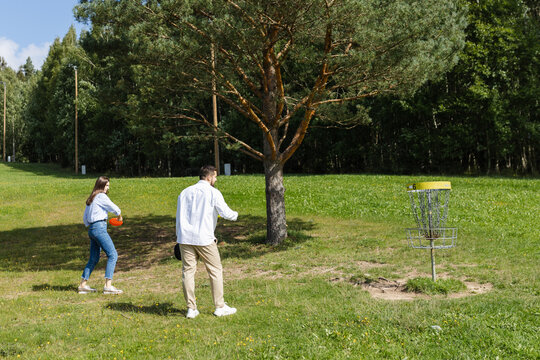 Venturous couple throwing discs at disc golf basket