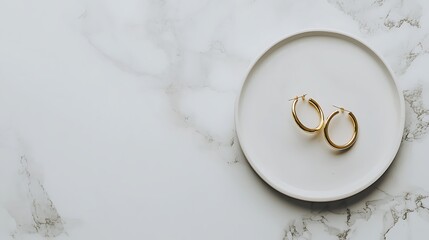 Gold hoop earrings on plate, marble background, jewelry display