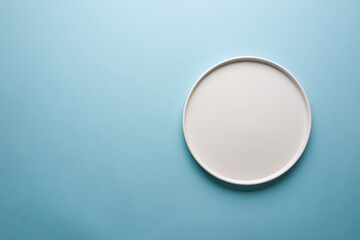 Top view of empty ceramic white plate on blue background