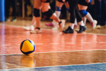 Naklejka premium Yellow Volleyball on Wooden Indoor Court with Players in Background — Dynamic Team Sports Scene