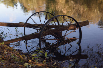 Part of an old broken cart with iron wheels on the river bank in the water.