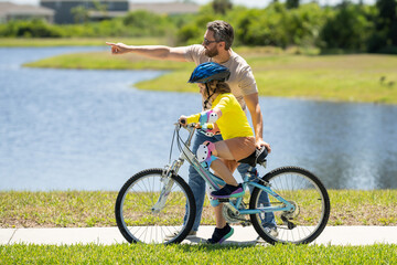 Fototapeta premium Sporty family father and son riding bike on a park. Child in safety helmet riding bike on summer day. Father teaching son riding on bike. Child son in bike helmet on bicycle. Fatherhood, Fathers day.