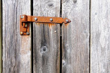 An aged wooden door showcases a weathered rusty hinge, capturing the beauty of decay and history in a quiet outdoor environment.