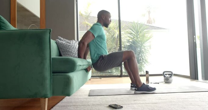 Strong and fit man doing tricep dips using sofa at home, exercising indoors