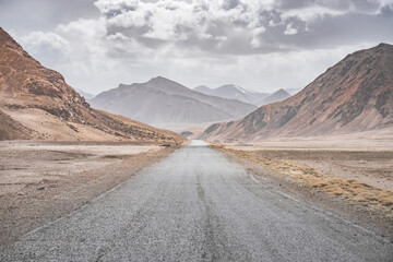 Asphalt road of the Pamir Highway in the valley of the Tien Shan Mountains in Tajikistan in the Pamirs, landscape in the high desert mountains for background, the road goes into the distance