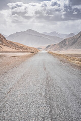 Asphalt road of the Pamir Highway in the valley of the Tien Shan Mountains in Tajikistan in the Pamirs, landscape in the high desert mountains for background, the road goes into the distance