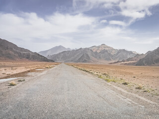 Asphalt road of the Pamir Highway in the valley of the Tien Shan Mountains in Tajikistan in the Pamirs, landscape in the high desert mountains for background, the road goes into the distance