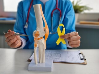 Therapist knee model holding yellow ribbon bone cancer concept
