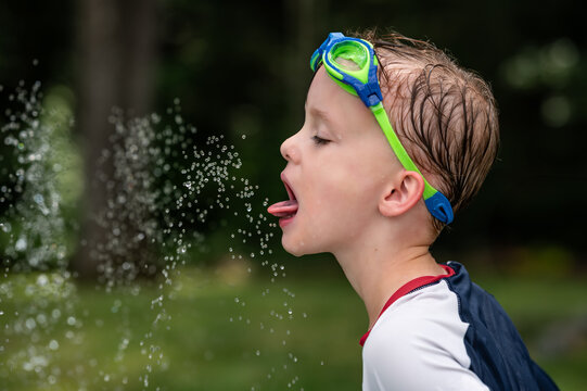Child wearing goggles, catching water droplets with his tongue
