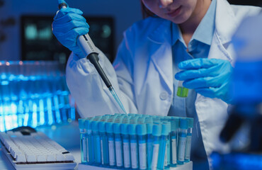 Medical scientist wearing lab coat and gloves using micropipette dropping blue liquid into test...