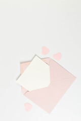 Top view of pink envelope, white card on white background. Valentine's day, pink hearts, love. Post flat lay, copy space.