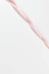Top view of pink ribbon on white background. Shiny rolled fabric, silk and satin material. Copy space.