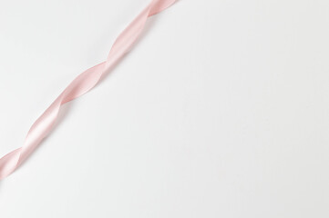 Top view of pink ribbon on white background. Shiny rolled fabric, silk and satin material. Copy space.