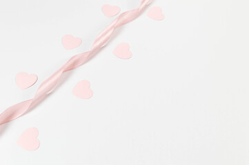 Top view of pink ribbon and pink hearts on white background. Valentine's day, love. Shiny rolled fabric, silk and satin material. Copy space, flat lay.