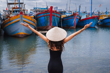 A female traveler wearing a traditional Vietnamese hat inspects traditional wooden boats at the...