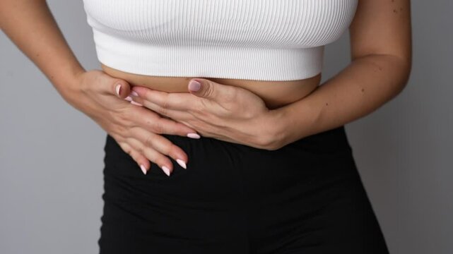 Young woman holding her side with her hands on a grey background. Sore side under the right rib. Stomach pain, diseases of the gallbladder and liver, attack of cholecystitis, gallstones. Slow motion