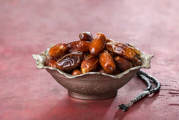 Bowl full of dates and  tasbih (misbaha) on old red-brown wooden table.