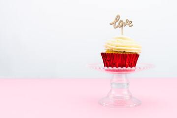 Valentine's Day. A cupcake with cream and red topping decoration with a wooden sign with the word LOVE on a pink background. Pastry bakery.