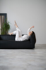 A cheerful woman relaxes on her sofa, dressed in cozy loungewear, showcasing her enjoyment in a calm home environment