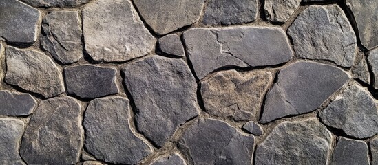 Fototapeta premium Textured surface of a stone wall made of irregularly shaped dark stones featuring natural variations and earth tones with Copy Space
