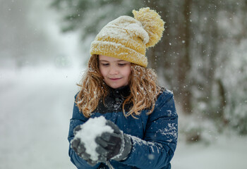 Winter kids portrait in snow. Kid winter face in snow. Happy Winter Children Holidays. Emotional Smiling Child Having Fun Playing with Snowflakes in Snow Park. Snow Falling in Winter Vacations.