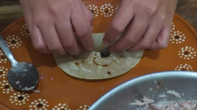 Female hands rolling tortillas with meat to prepare enchiladas or flute tacos.