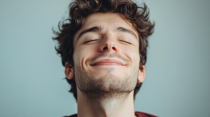Fototapeta premium Portrait of a young man with curly hair smiling softly against a muted background with Copy Space for text.