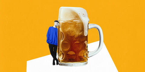 Man wearing blue sweatshirt leaning against oversized beer mug with foam spilling over rim against...