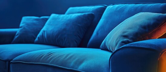Obraz premium Elegant close-up of a luxurious blue velvet sofa with plush cushions illuminated by vibrant neon lighting in a contemporary living space